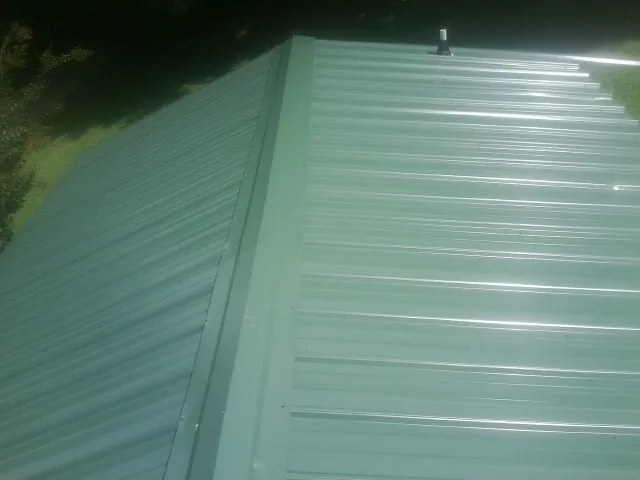 New green metal panels meeting at the ridge of a roof — Flat Roof Repair work by our crew in Macclenny
