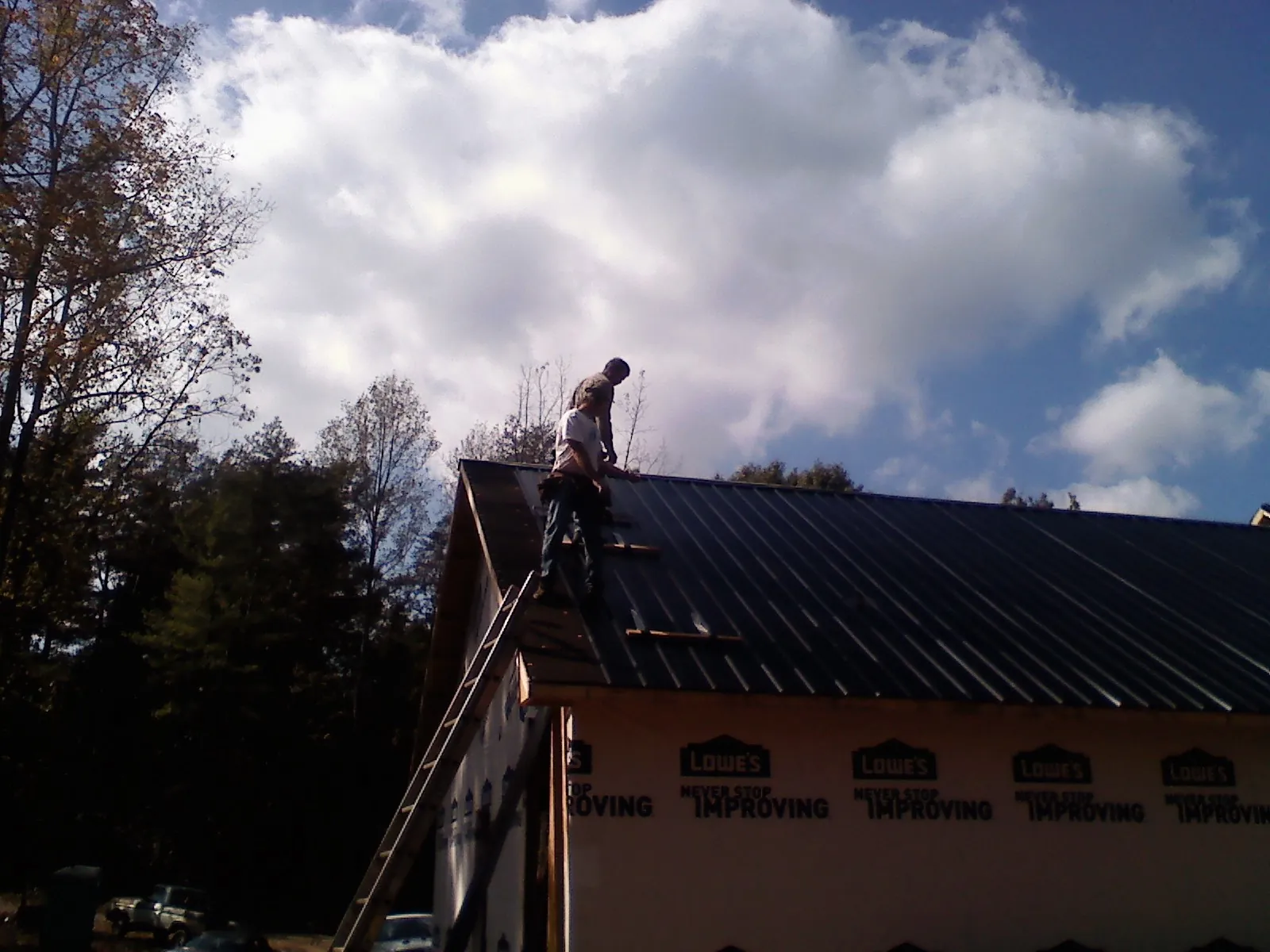 Roofer fastening dark metal panels high against a cloudy sky, from a Roof Inspection job in Macclenny